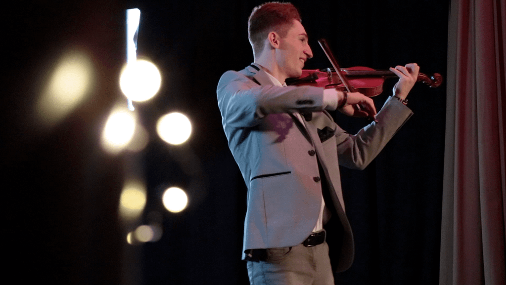 Paul Kolodziej (musical artist and violinist) plays the violin on stage with light bulbs in the front